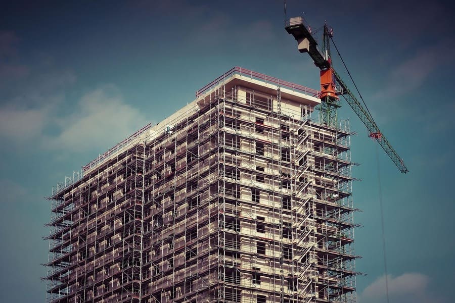 Edificio de 12 plantas en construcción. A su derecha figura una grúa de obras. Cielo azul grisáceo de fondo