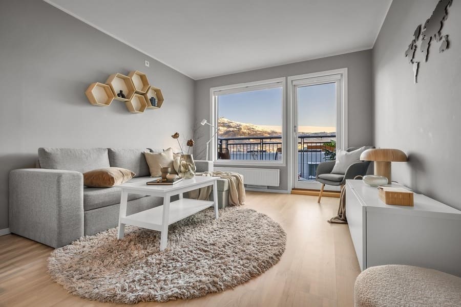 salón de una casa veraniega. Ambient calro y decoración en colores blancos y beige. Al fondo, ventanal que da a un balcón con vistas a un escenario limpio, con cielo