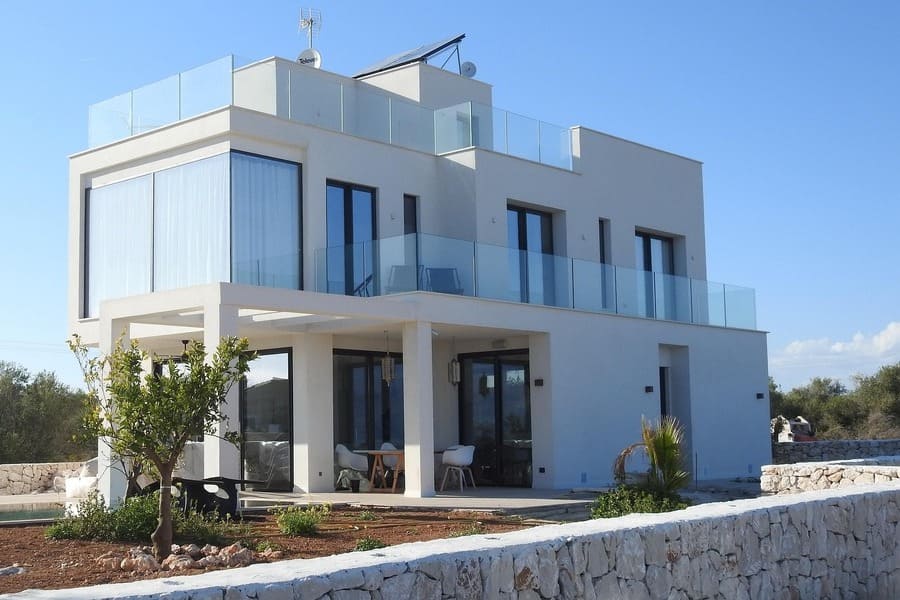 foto de chalet blanco de dos plantas, con abundantes ventanas. Jardín alrededor y cielo azul